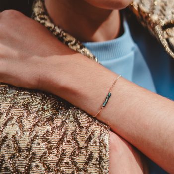 Model draagt Petrol & gold bracelet (armband met petrol kraaltjes) bij een goudkleurige brokaatjas